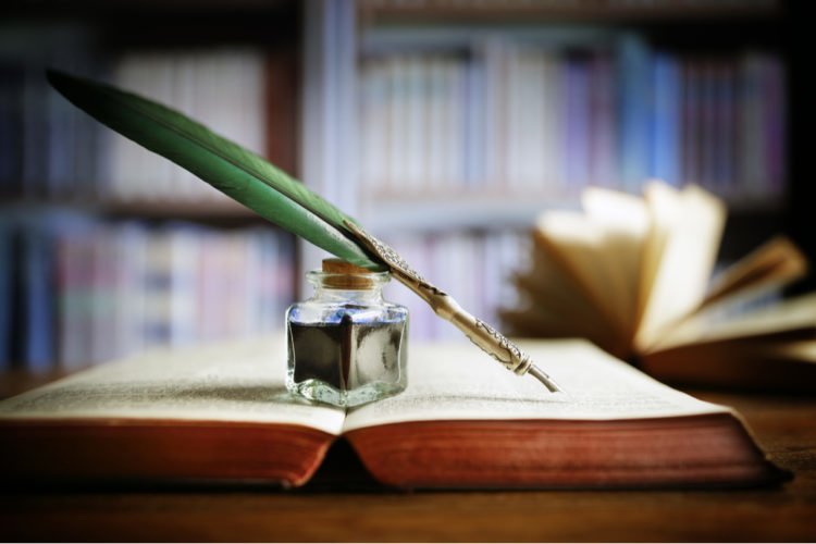 open book with green quill and ink jar